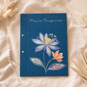 Könnte beinhalten: Eine dunkelblaue Mappe mit zwei silbernen Metallschrauben an der linken Seite. Der Einband zeigt eine Blumenillustration mit einer großen violett-gelben Blüte, einer kleineren orangefarbenen Blüte und gemusterten Blättern. Der Text "Meine Zeugnisse" ist in Weiß aufgedruckt.