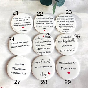 May include: A collection of white, round buttons with black text and red heart accents. Each button features a different German phrase or quote. Some buttons include the name "Julia Engelmann".