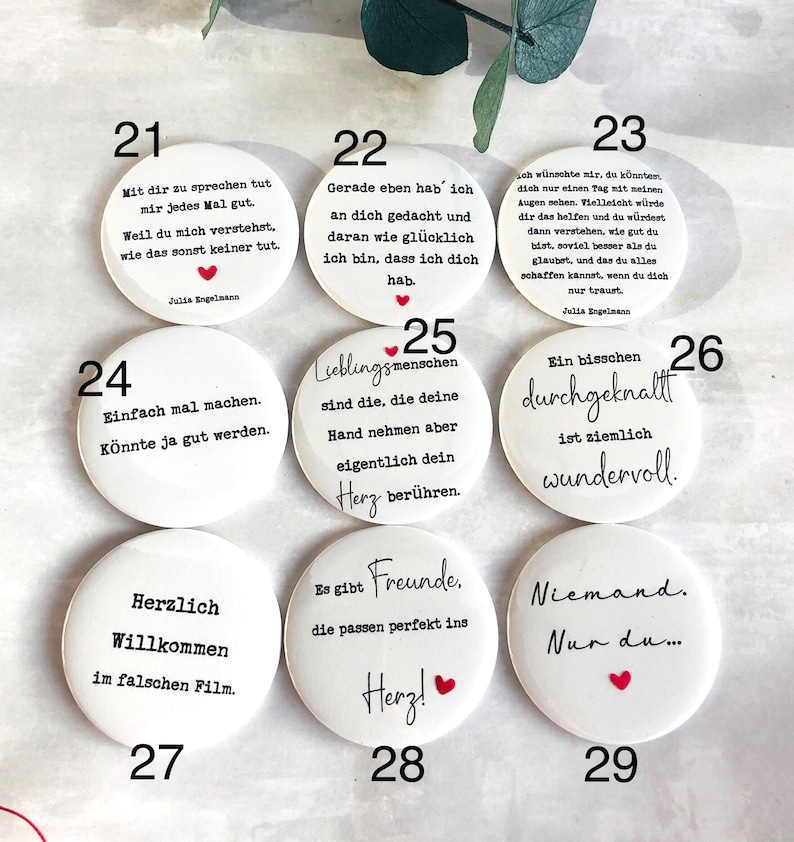 May include: A collection of white, round buttons with black text and red heart accents. Each button features a different German phrase or quote. Some buttons include the name "Julia Engelmann".