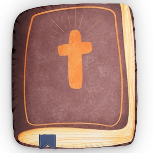 May include: A brown book-shaped pillow with a yellow spine and a large orange cross on the front. The cross has a sunburst design behind it.