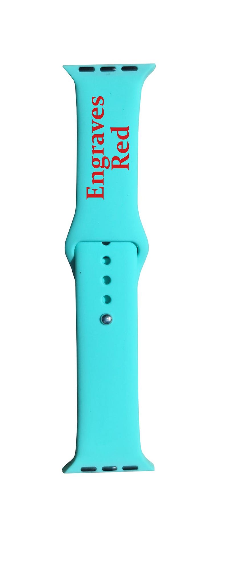 以下が含まれることがあります： 赤色の「Engraves Red」の文字が縦にプリントされた、ターコイズブルーの時計バンド。バンドにはピンと3つの調整穴があります。