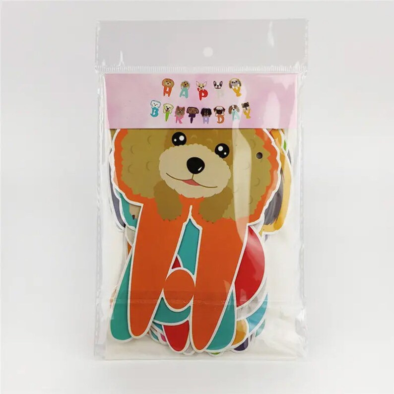 Puede incluir: Una bolsa de pl&aacute;stico que contiene un conjunto de decoraciones de fiesta de tem&aacute;tica canina de colores vivos. Las decoraciones incluyen una pancarta que dice "Feliz cumplea&ntilde;os" y varias formas de perros recortadas.