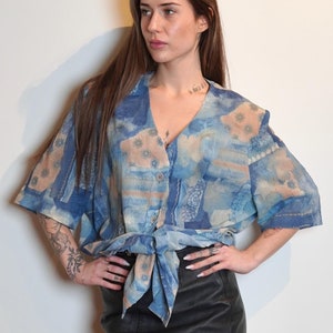 May include: A woman wearing a blue and white patterned blouse tied at the waist with a black leather skirt and brown cowboy boots.