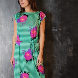 Könnte beinhalten: Ein grün-weiß gestreiftes Kleid mit einem Blumendruck in den Farben Pink, Lila und Schwarz. Das Kleid hat einen Bindegürtel in der Taille und kurze Ärmel.