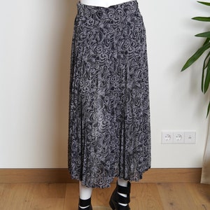 May include: A black and gray pleated skirt with a floral pattern. The skirt is midi length and has a high waist.