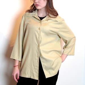 Może przedstawiać: Jasnobeżowa koszula zapinana na guziki, o długim, luźnym kroju i kołnierzyku. Koszula ma lekko oversizowy krój i zapinana jest na guziki.