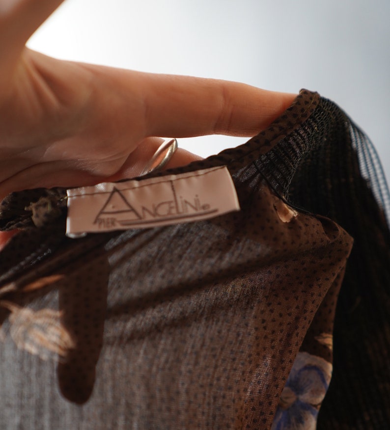 May include: Close-up of a brown sheer fabric with a black polka dot pattern. The fabric has a label that reads "Per Angeline."