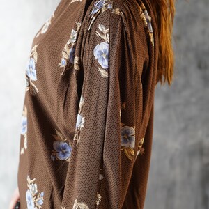 May include: A brown long-sleeved dress with a floral print featuring blue and white flowers. The dress has a gathered detail at the shoulders.