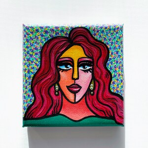 May include: A square canvas painting featuring a stylized portrait of a woman. The woman has red hair, gold earrings, and a green top. The background is a colorful pattern of blue, purple, and yellow dots.