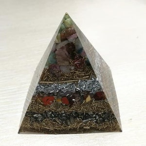 Può includere: Una piramide di vetro trasparente riempita con vari cristalli colorati e scaglie metalliche. La piramide è un oggetto popolare per l'arredamento della casa e le pratiche spirituali.