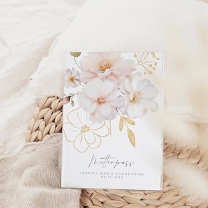 Könnte beinhalten: Eine weiße Karte mit einem floralen Design in Rosa- und Goldtönen. Der Text "Mutterpass" ist in schwarzer Kursivschrift geschrieben. Unter dem Text steht der Name "JESSICA MARIA SCHNEYDERN" und das Datum "05.11.1995".