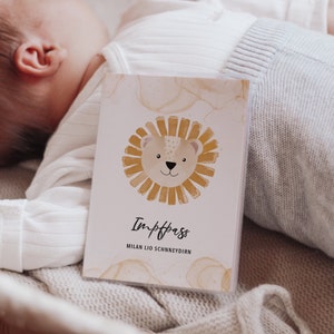 May include: A white card with a watercolor illustration of a lion's face with a yellow mane. The text "Impfpass" and "MILAN LIO SCHNEYDIRN" is printed on the card.