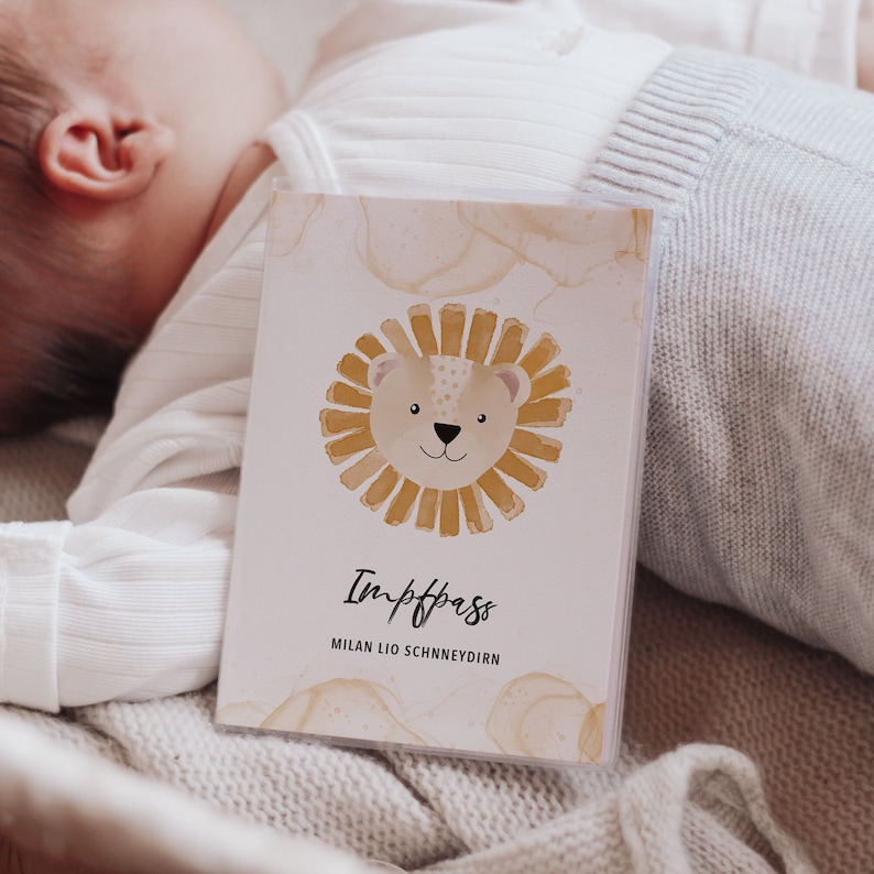 May include: A white card with a watercolor illustration of a lion's face with a yellow mane. The text "Impfpass" and "MILAN LIO SCHNEYDIRN" is printed on the card.