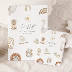 May include: Two white photo albums with a boho theme. The covers feature illustrations of animals, rainbows, and a sun. The text on the covers reads "U-Heft" and "Impfpass" with the name "LENI SCHNEYDIRN" and the date "16.06.2023".
