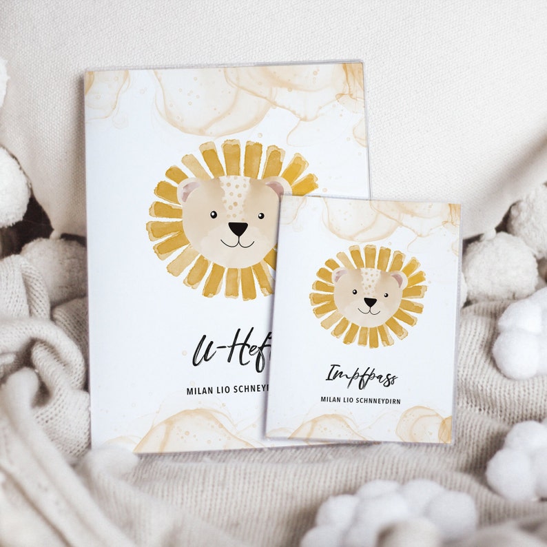 May include: Two watercolor lion-themed cards with a white background and brown watercolor accents. The larger card says "U-Heft" and "MILAN LIO SCHNEYDERN". The smaller card says "Impfpass" and "MILAN LIO SCHNEYDERN".