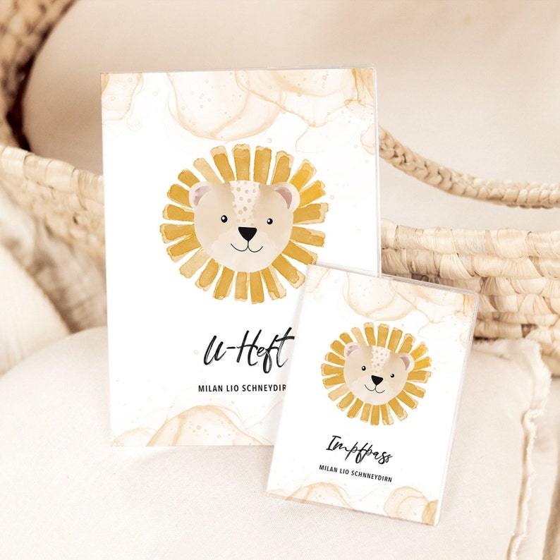 May include: Two white cardstock covers with a watercolor background and a cartoon lion illustration. The larger cover says "u-Heft" and "MILAN LIO SCHNEYDIR". The smaller cover says "Impfpass" and "MILAN LIO SCHNEYDIR".