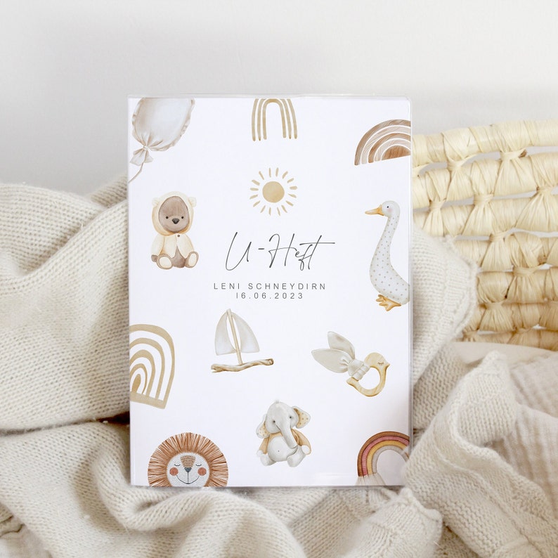 May include: A white card with a brown and white bear, a sun, a sailboat, a bird, an elephant, a lion, and a rainbow. The card says "U-H&auml;tt" and "LENI SCHNEYDIRN 16.06.2023".
