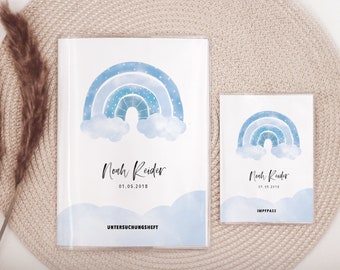 May include: Two blue and white rainbow themed baby record books. The larger book is labeled "Untersuchungsheft" and the smaller book is labeled "Impfpass". Both books feature the name "Noah Reider" and the date "01.05.2018".