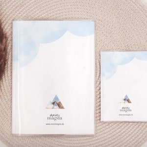 May include: Two clear acrylic frames, one large and one small, each containing a white print. The prints feature a blue watercolor cloud design at the top and a mountain illustration. The text "mein magda" and website address are at the bottom.