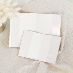 May include: Two white blank notebooks with a subtle striped pattern. The notebooks are lying on a beige textured fabric.