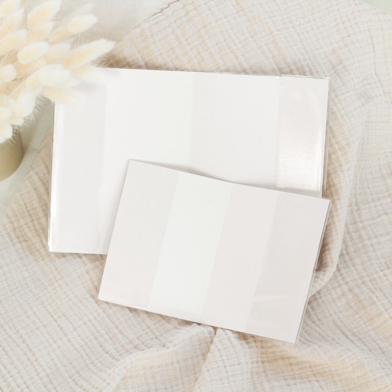 May include: Two white blank notebooks with a subtle striped pattern. The notebooks are lying on a beige textured fabric.