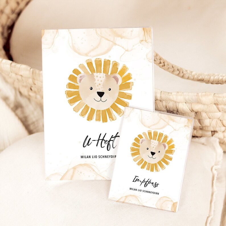 May include: Two small, white, rectangular notebooks with a watercolor lion illustration. The top notebook says "u-heft" and "MILAN LIO SCHNEYDIP". The bottom notebook says "Impfpass" and "MILAN LIO SCHNEYDIPP".