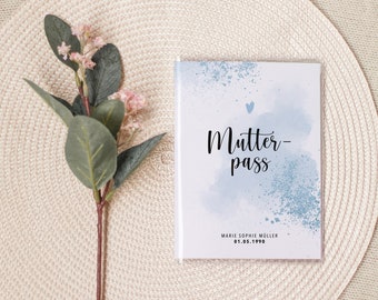 May include: A blue and white watercolor-style cover for a "Mutter-pass" book. The cover features a small heart and the text "Mutter-pass" in black. The name "Marie Sophie Muller" and the date "01.05.1990" are printed in black at the bottom of the cover.