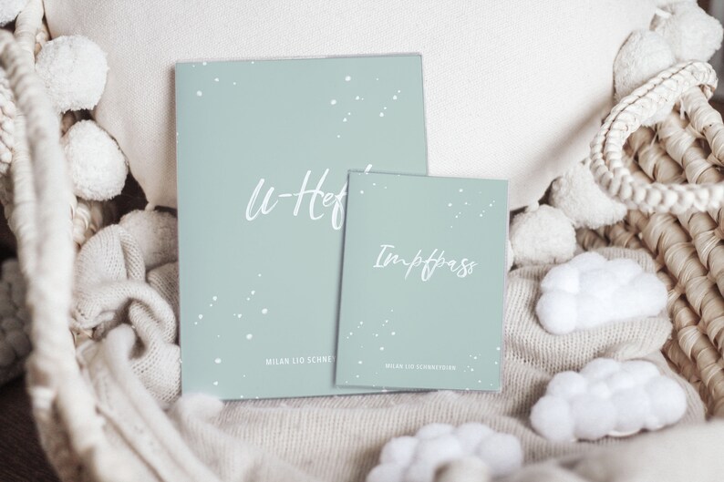 Puede incluir: Dos libros de registro para beb&eacute;s de color azul claro con texto blanco. El libro m&aacute;s grande dice "U-Heft" y el libro m&aacute;s peque&ntilde;o dice "Impfpass". Ambos libros tienen un patr&oacute;n de estrellas blancas.