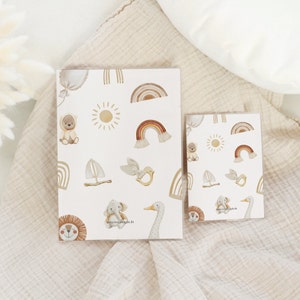May include: Two printable sheets with a white background and a repeating pattern of illustrations. The illustrations include a sun, a rainbow, a sailboat, a bird, a bear, an elephant, a lion, and a goose. The text "www.mejsjilda.de" is printed on the sheets.