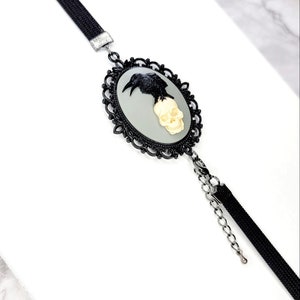 May include: Black choker necklace with a silver chain and a cameo featuring a black raven perched on a white skull.