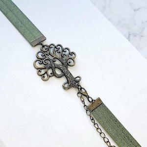May include: A green fabric bookmark with a metal tree of life charm and a heart-shaped charm on a chain.