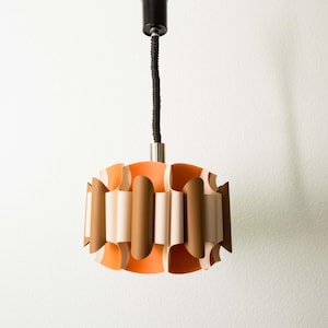 May include: A retro pendant light fitting. The light has a cylindrical shape with alternating orange, brown, and off-white vertical panels. It hangs from a black cord and a silver-toned metal base, a classic design.