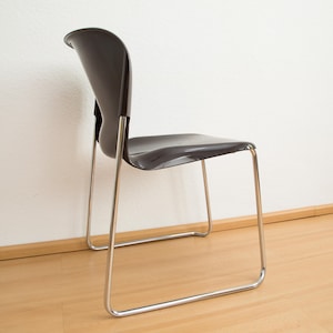 May include: A black plastic chair with a chrome frame. The chair is sitting on a wooden floor.