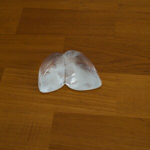 May include: Two clear ice cubes shaped like a heart on a wooden surface.