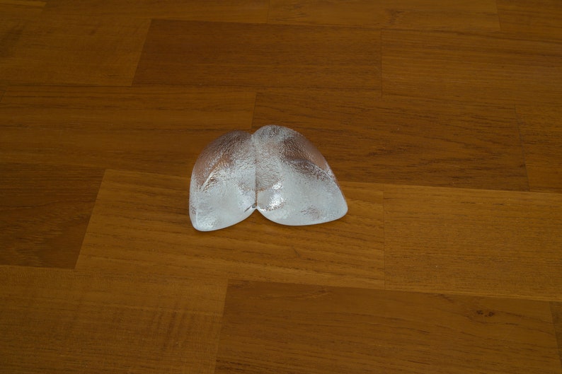 May include: Two clear ice cubes shaped like a heart on a wooden surface.