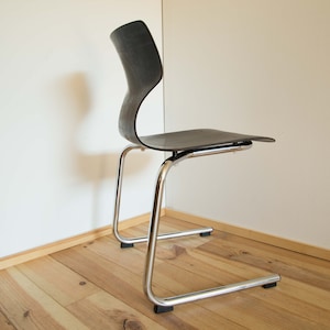 May include: A black and chrome chair with a curved back and a chrome base. The chair is sitting on a wooden floor.