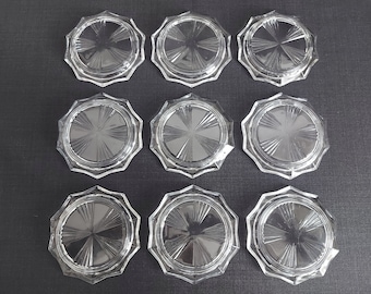 May include: Ten clear glass coasters with a starburst design. The coasters are octagonal in shape and have a raised edge.