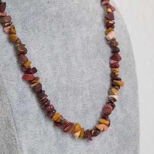 Peut inclure: Un collier composé de pierres rouges, brunes et jaunes. Le collier est sur un présentoir en velours gris.