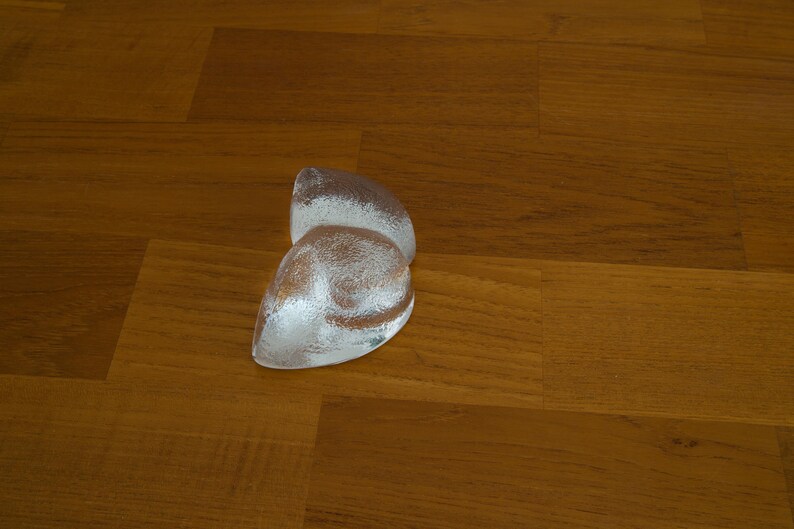 May include: A pair of clear glass paperweights in the shape of a heart, sitting on a wooden surface.