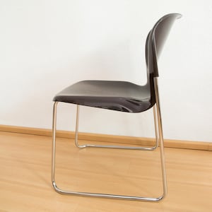 May include: A dark gray plastic chair with a chrome frame. The chair has a curved back and a simple design.