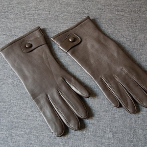 Puede incluir: Un par de guantes de cuero marrón con cierre de botón en la muñeca.