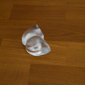 May include: Two silver teardrop-shaped glass sculptures on a wooden surface.