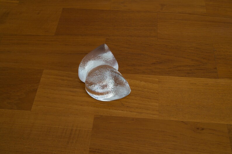 May include: Two silver teardrop-shaped glass sculptures on a wooden surface.