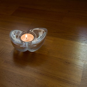 May include: A clear glass candle holder shaped like a butterfly with a lit tea light candle inside.