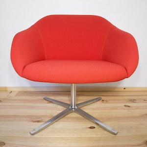Puede incluir: Una silla giratoria roja con una base cromada y cuatro patas. La silla está tapizada en un tejido suave de color rojo.