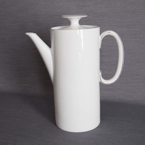 Op de afbeelding: Witte koffiekan van keramiek met een zilveren deksel en handvat.