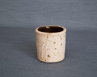 Può includere: Un piccolo vaso in ceramica beige con una superficie ruvida e testurizzata e un interno smaltato marrone.