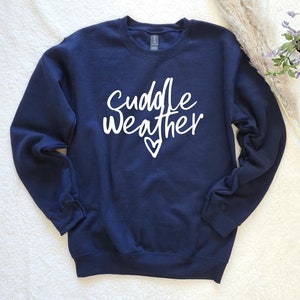 May include: Navy blue sweatshirt with the words "Cuddle Weather" in white script, along with a small heart. The sweatshirt is a crew neck style, with long sleeves.