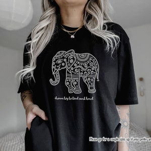 May include: A black t-shirt featuring a white graphic of an elephant decorated with intricate floral and geometric patterns. Below the elephant, the text reads "dream big be kind work hard". The bottom right corner includes the text "Please go for a couple sizes up if you prefer an oversized fit".