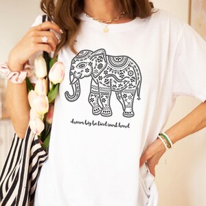May include: A white short-sleeve t-shirt featuring a black graphic of an elephant decorated with intricate patterns. Below the elephant, the text reads, dream big be kind work hard. The design is printed in black ink on the front of the shirt.